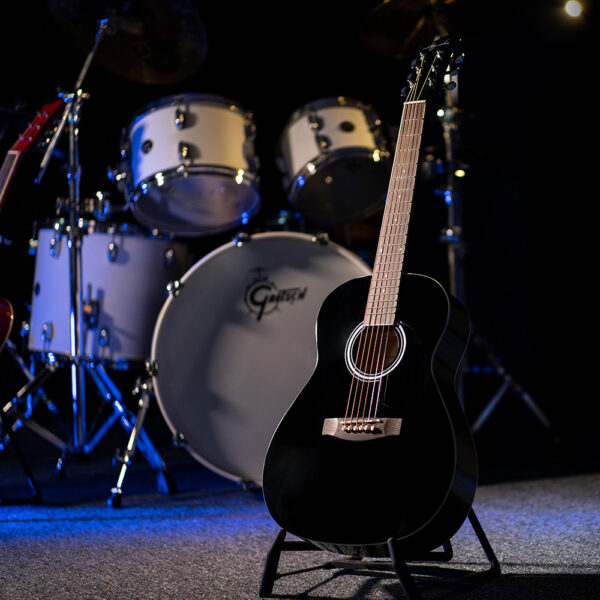 black JJ43 acoustic guitar on stand in front of drum set