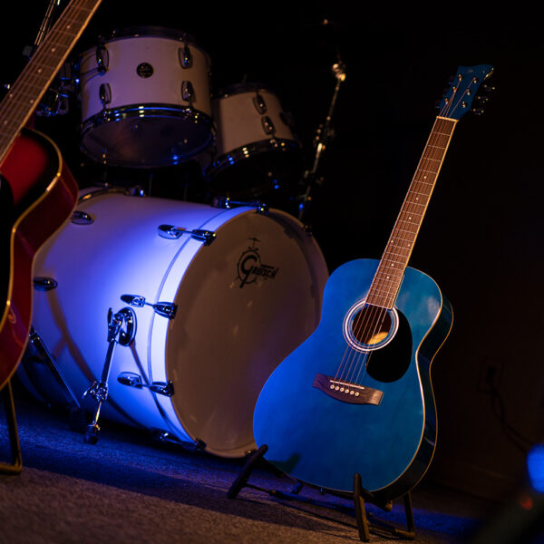 JJ43 acoustic guitar on stand in front of drum set